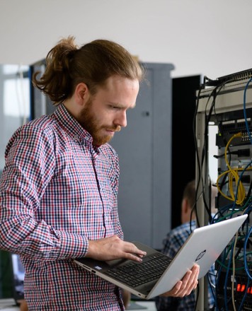 man working on a laptop in front of a server rack